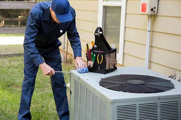 Technician inspecting a residential outdoor condenser beside a home in East Aurora New York