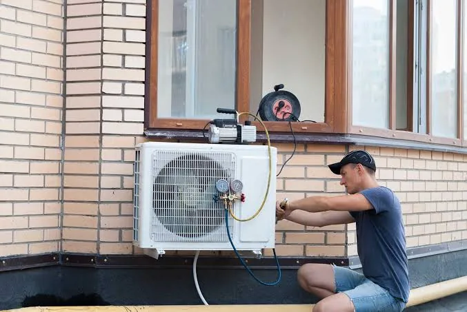 Technician installing a residential mini-split air conditioner on a brick home