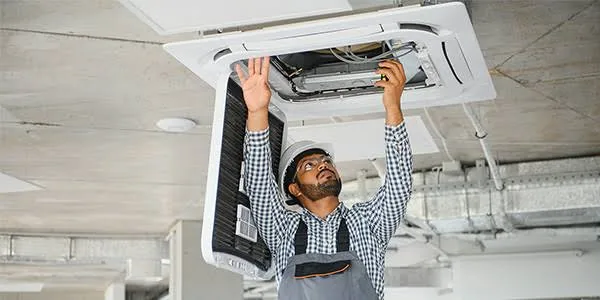 Technician inspecting a ceiling HVAC cassette and indoor airflow equipment