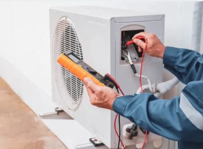 Technician testing electrical connections on an outdoor HVAC unit